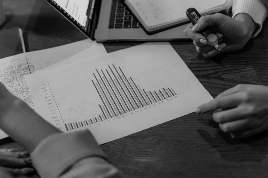 Femme d'affaires analysant des graphiques financiers sur smartphone avec ordinateur portable et documents.